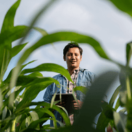 Man standing among tall crops, smiling.