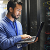 A man standing working on a computer he is holding in his hand