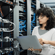 A woman working on a laptop in a server room